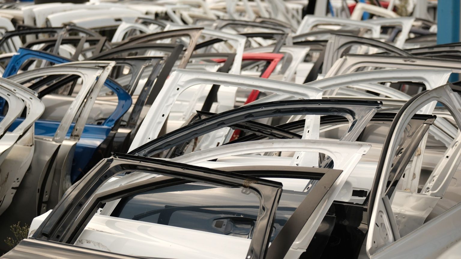 Portas de carros de diferentes cores dispostas em um desmanche de veículos.