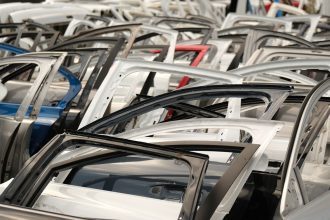 Portas de carros de diferentes cores dispostas em um desmanche de veículos.