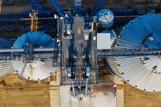 Vista aérea de silos industriais de armazenamento de grãos ao lado de trilhos ferroviários.