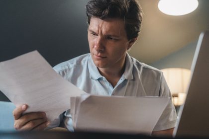 Homem sentado analisa documentos em um ambiente de trabalho.